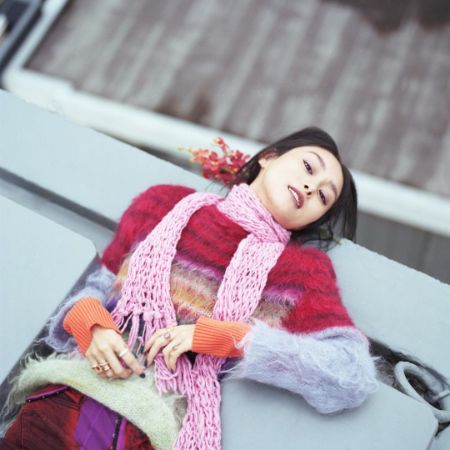 Shioli Kutsuna is posing by sitting on a bench wearing warm clothes.